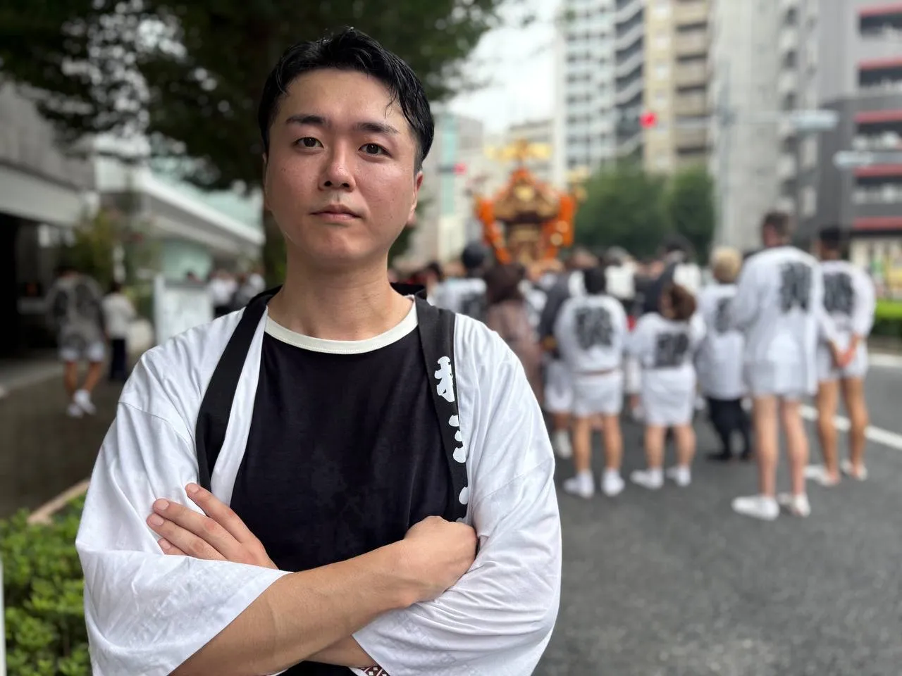法被を着て腕を組む高橋。背景に神輿と担ぎ手